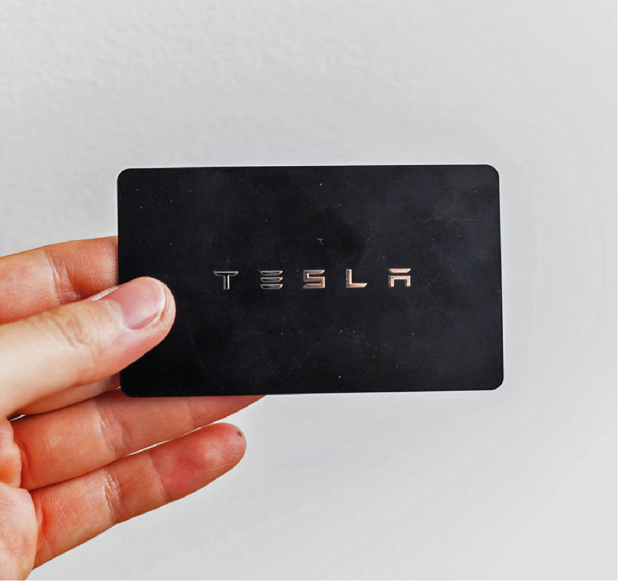 Hand holding Tesla card in black with gold writing 