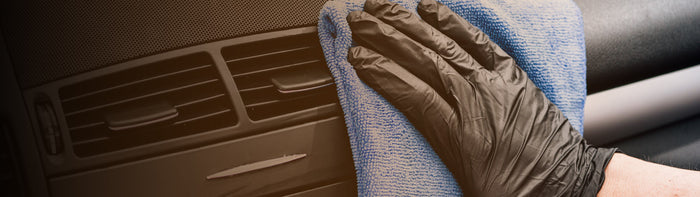 Person wearing black glove holding blue cloth wiping inside of car 
