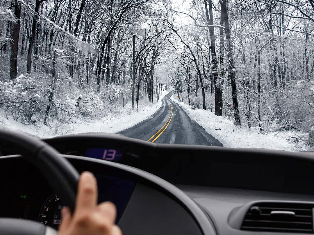 Hands on steering wheel in car driving on Winter road with snow and ice