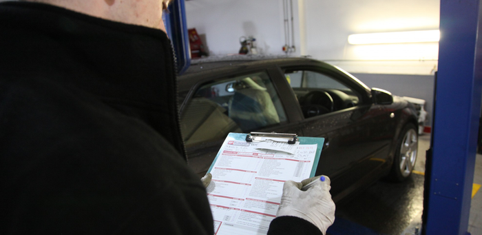 Mechanic back reading checklist and car in background 